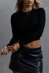 A woman wearing a long sleeve black crop top with a crew neckline and a black mini skirt.