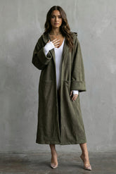 Woman wearing a long olive green coat against a gray background
