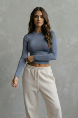 Woman wearing a blue long-sleeve top and beige pants against a gray background