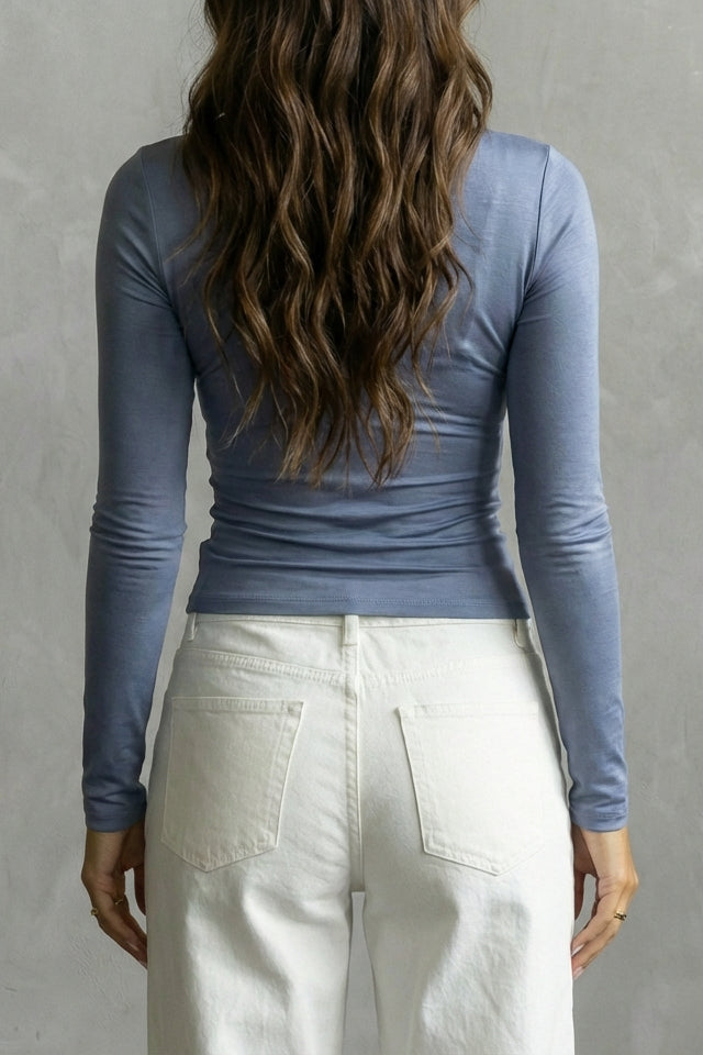 Person wearing a blue long-sleeve top and white pants against a gray background