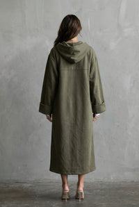 Person wearing a green coat standing against a gray wall