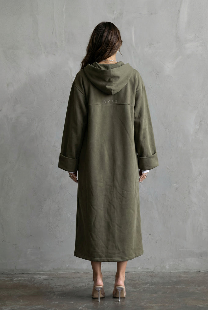 Person wearing a green coat standing against a gray wall