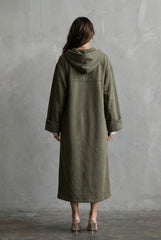 Person wearing a green coat standing against a gray wall