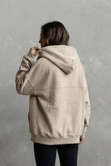 Person wearing a beige hoodie and black leggings against a gray background
