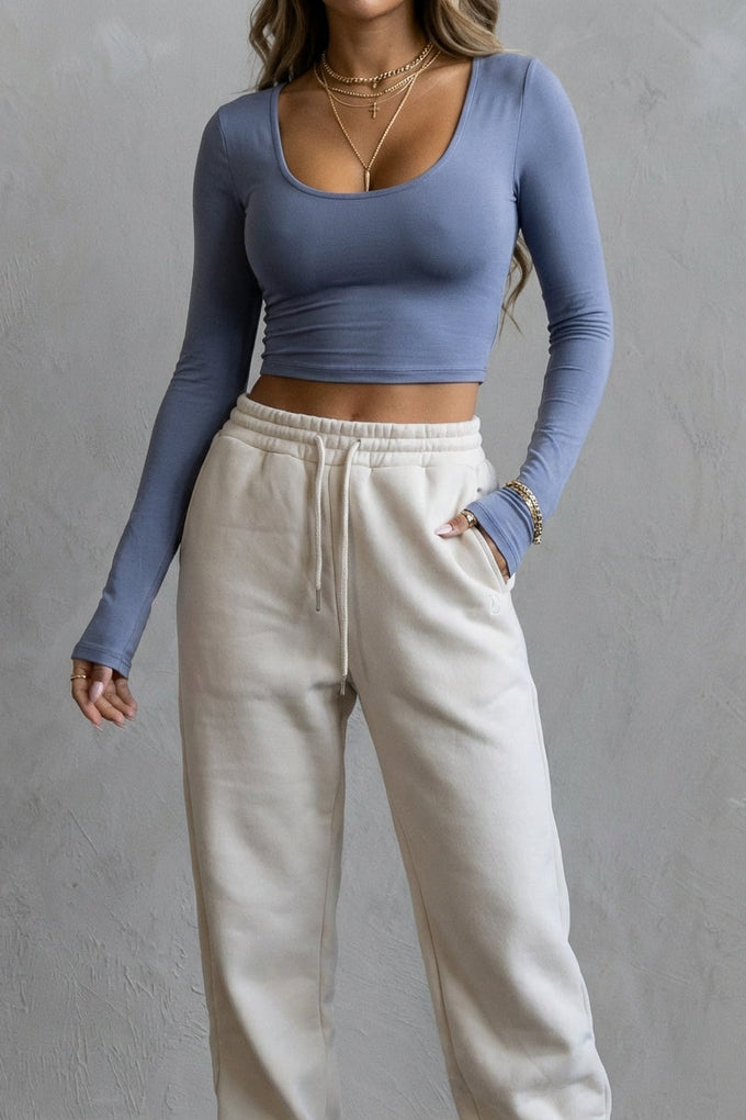 blue long-sleeve crop top and beige sweatpants against a gray background