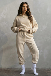 Woman wearing a beige hoodie and jogger set against a gray background