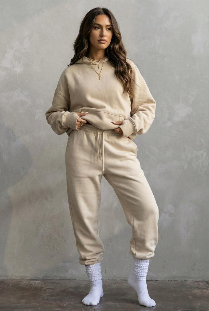 Woman wearing a beige hoodie and jogger set against a gray background