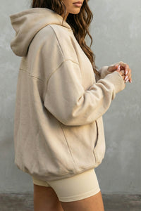 Person wearing a beige hoodie and white shorts against a gray background