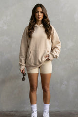 Woman wearing a beige hoodie and shorts set against a gray background
